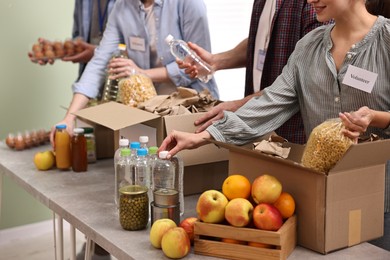 Photo of Group of volunteers packing food donations at table indoors, closeup