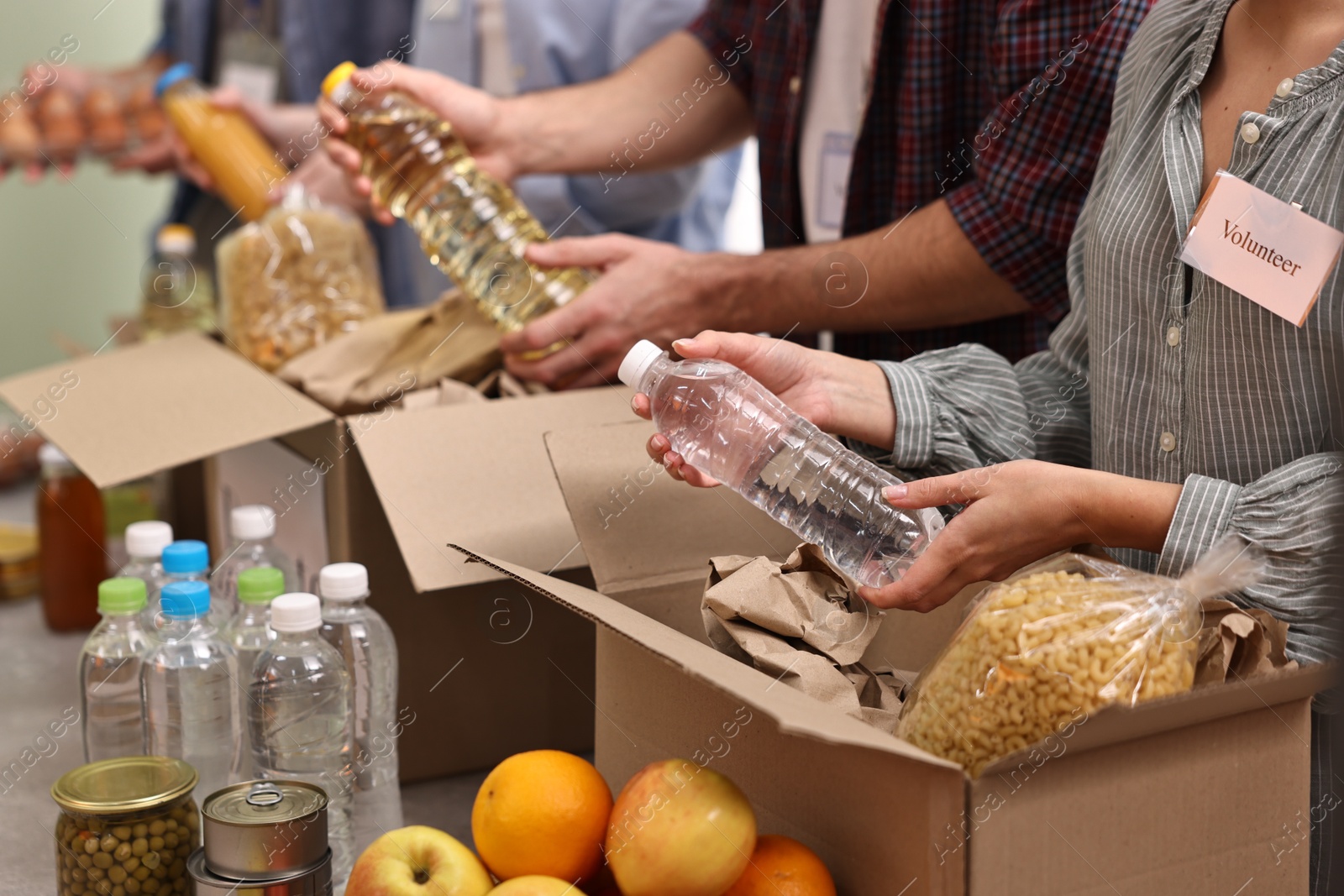 Photo of Group of volunteers packing food donations at table indoors, closeup