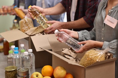 Photo of Group of volunteers packing food donations at table indoors, closeup