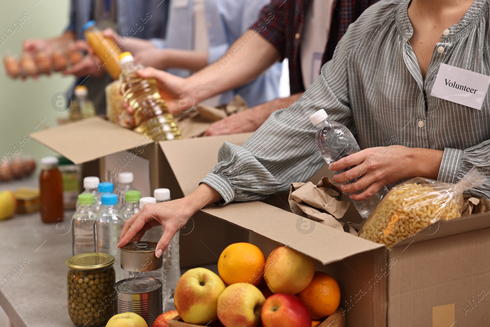 Photo of Group of volunteers packing food donations at table indoors, closeup