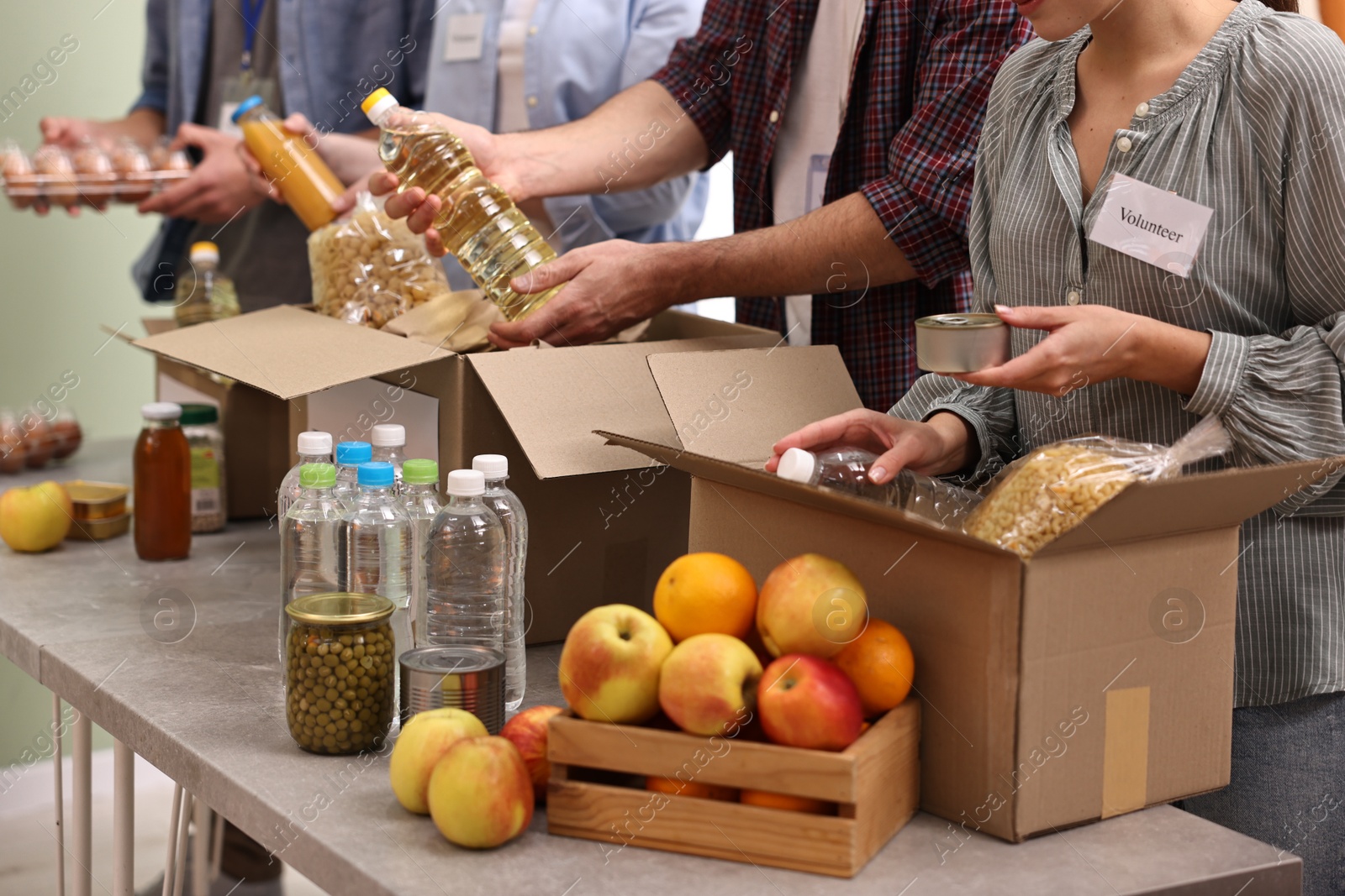 Photo of Group of volunteers packing food donations at table indoors, closeup