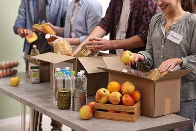 Photo of Group of volunteers packing food donations at table indoors, closeup