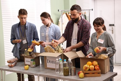 Photo of Group of volunteers packing food donations at table indoors