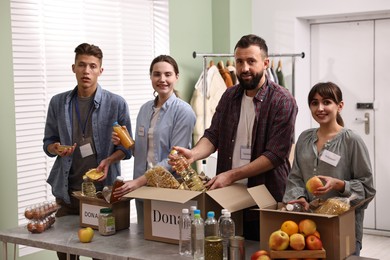 Photo of Group of volunteers packing food donations at table indoors