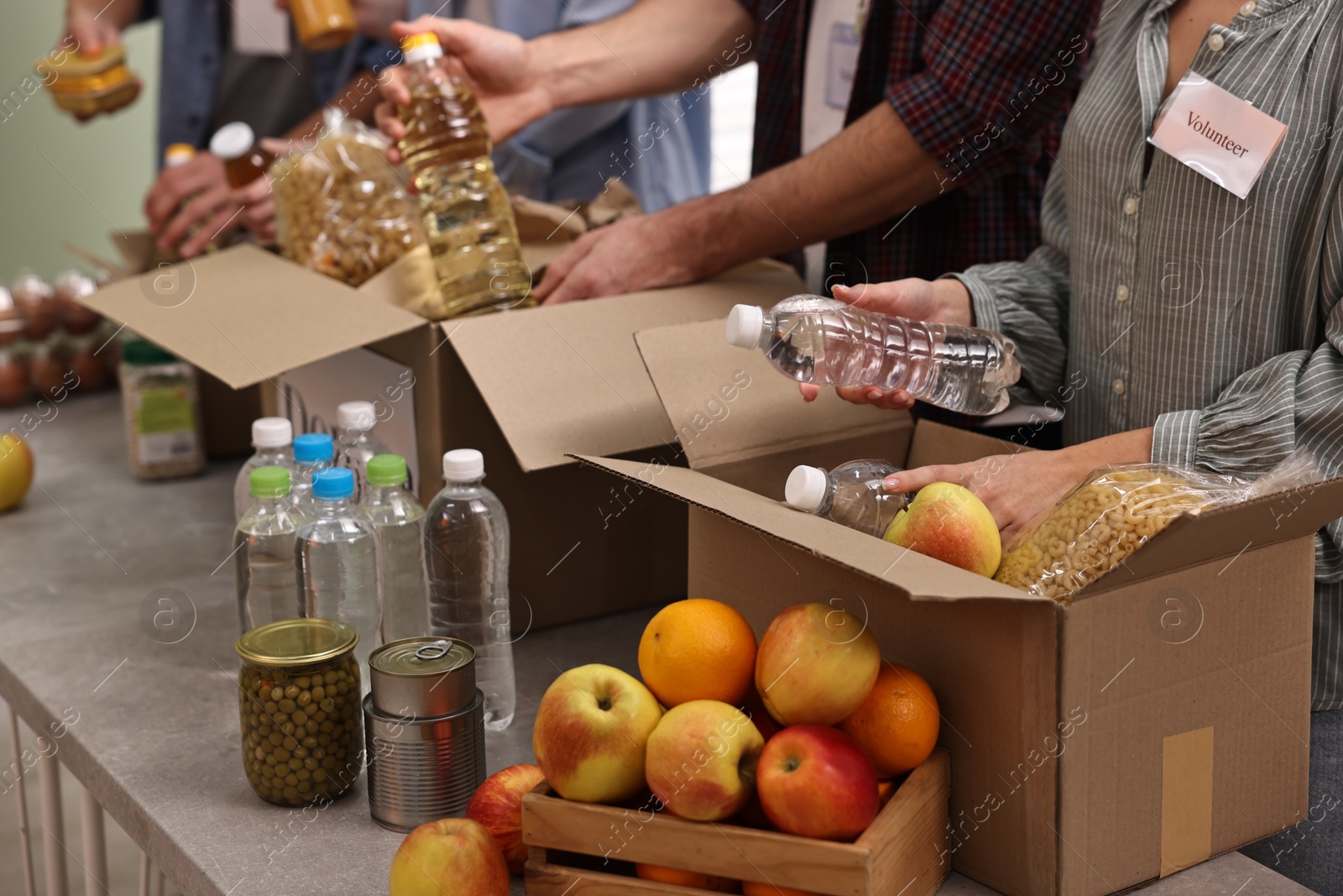 Photo of Group of volunteers packing food donations at table indoors, closeup