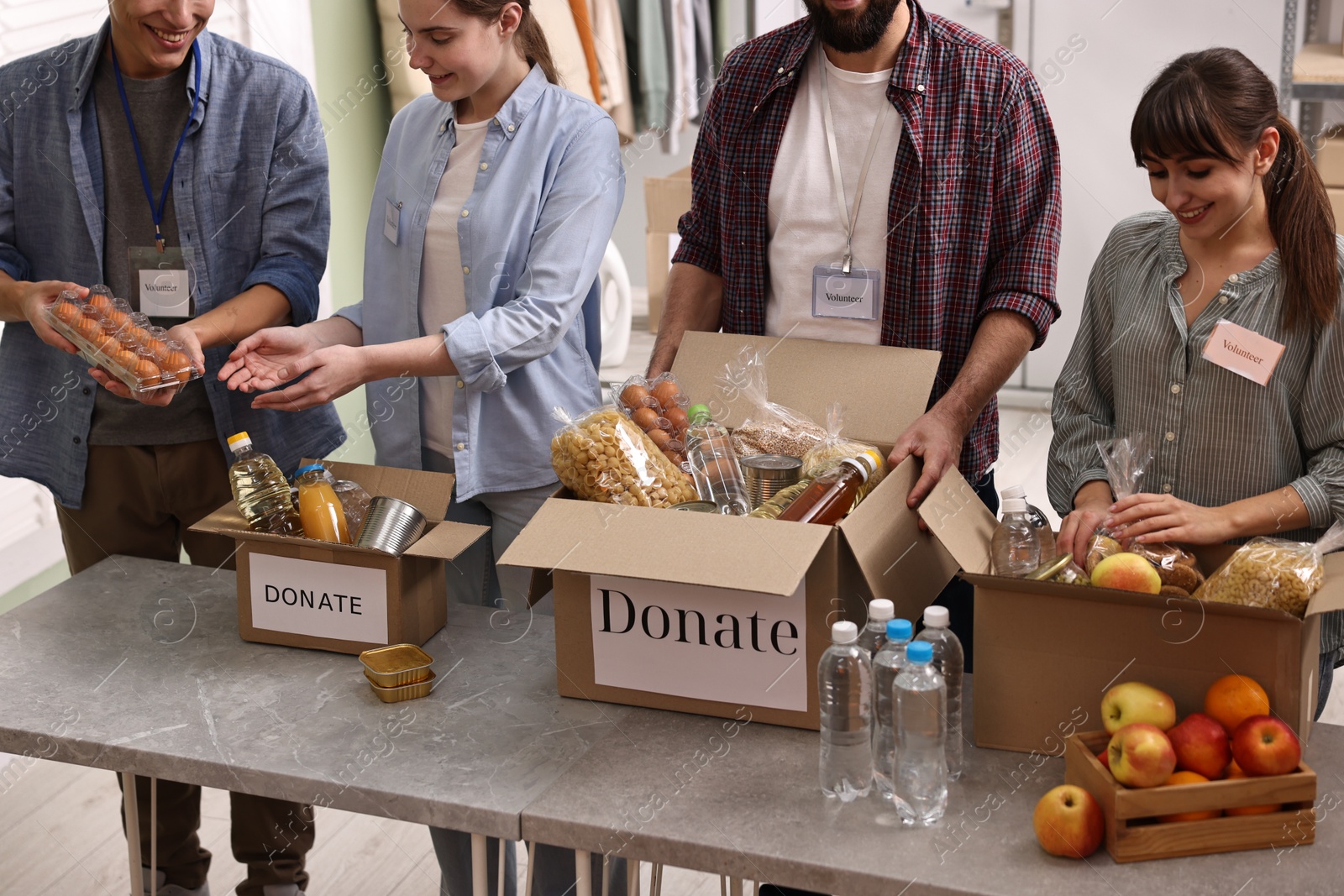 Photo of Group of volunteers packing food donations at table indoors, closeup