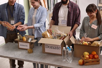 Photo of Group of volunteers packing food donations at table indoors, closeup