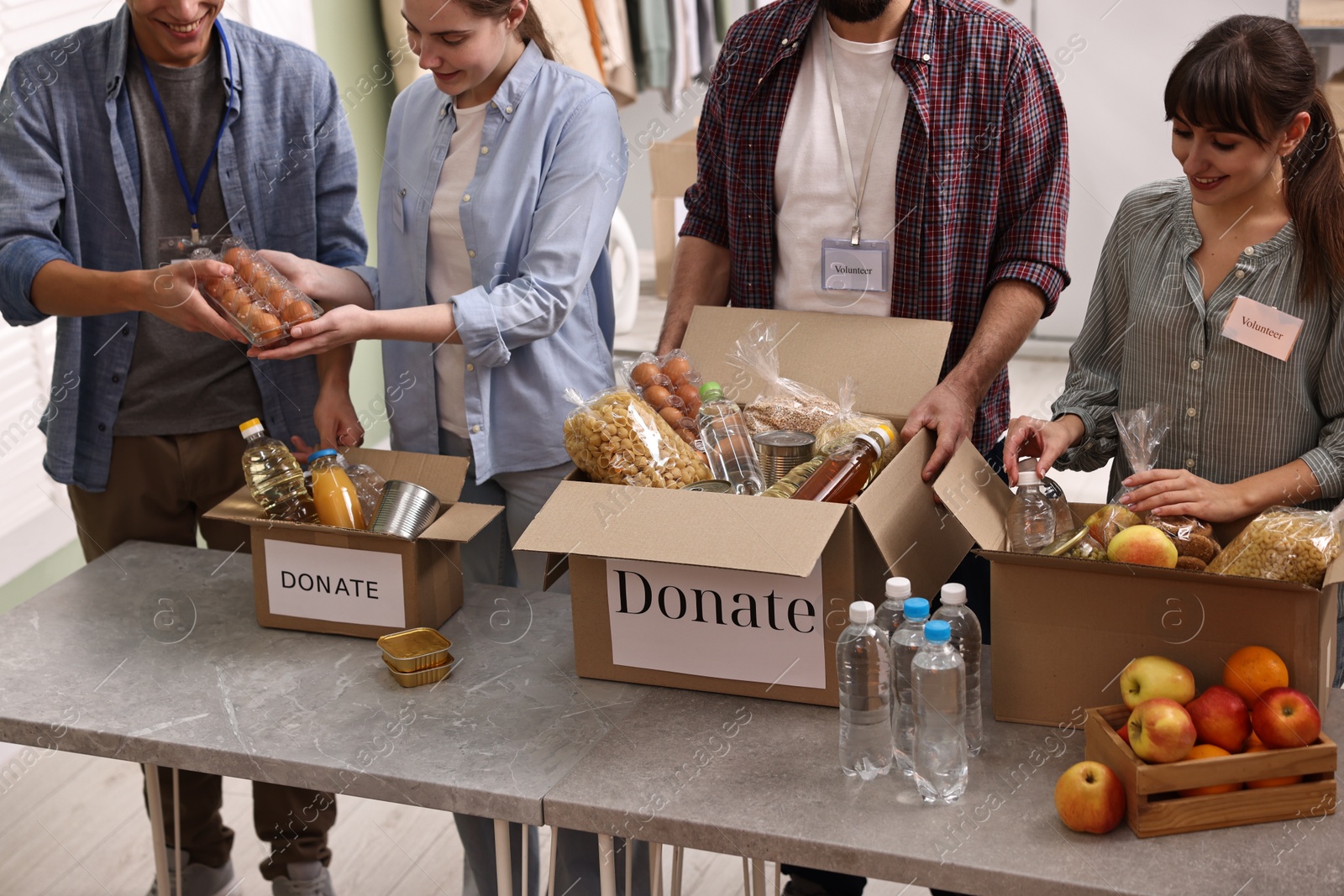 Photo of Group of volunteers packing food donations at table indoors, closeup