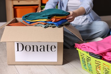 Photo of Volunteer putting clothes into donation box on floor indoors, closeup