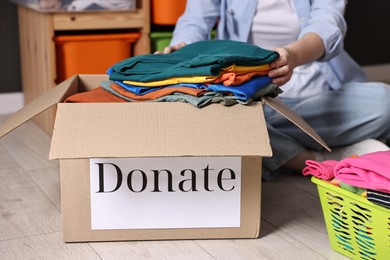 Photo of Volunteer putting clothes into donation box on floor indoors, closeup