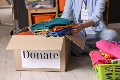 Photo of Volunteer putting clothes into donation box on floor indoors, closeup