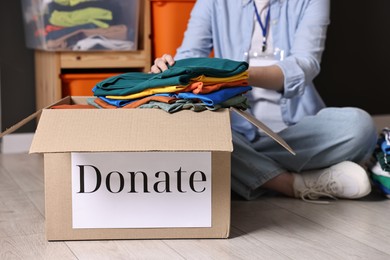 Photo of Volunteer putting clothes into donation box on floor indoors, closeup