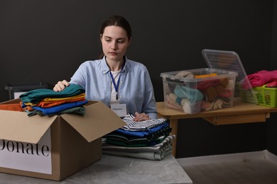 Photo of Volunteer putting clothes into donation box at table indoors, space for text