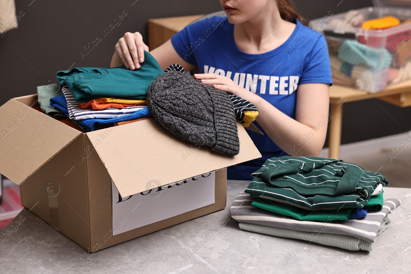 Photo of Volunteer putting clothes into donation box at table indoors, closeup