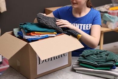 Photo of Volunteer putting clothes into donation box at table indoors, closeup