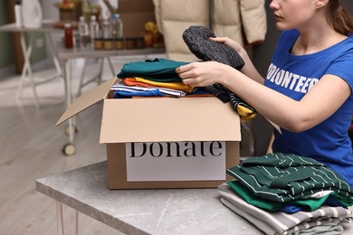 Photo of Volunteer putting clothes into donation box at table indoors, closeup