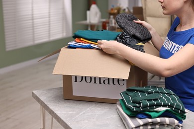 Photo of Volunteer putting clothes into donation box at table indoors, closeup