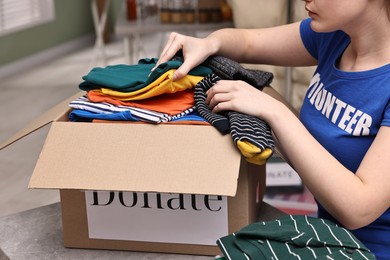 Photo of Volunteer putting clothes into donation box at table indoors, closeup