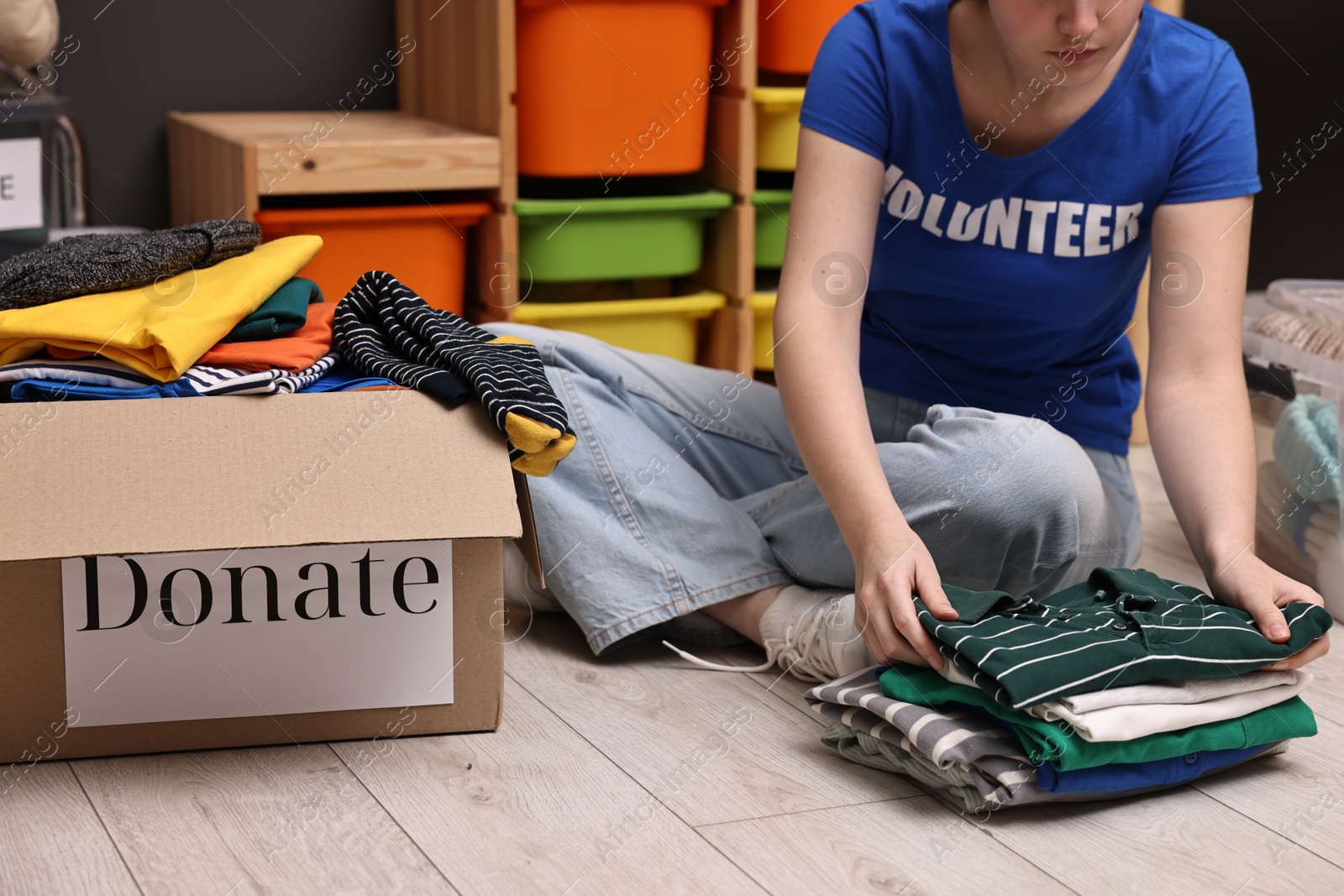 Photo of Volunteer sorting clothes for donation on floor indoors, closeup