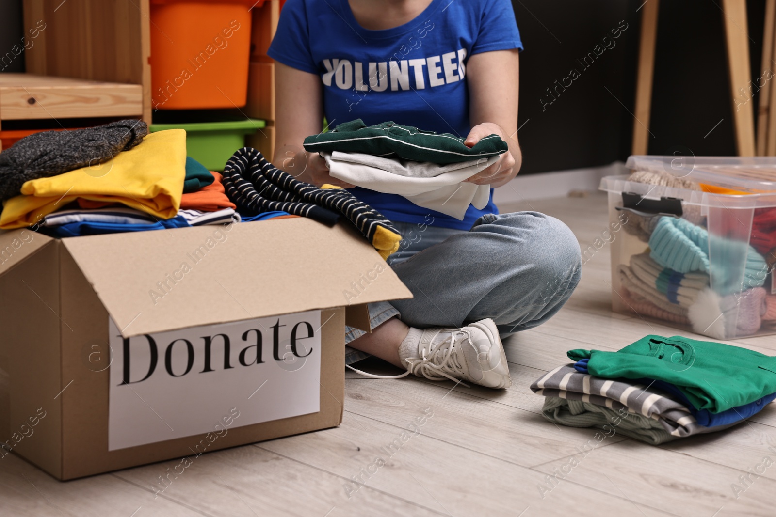 Photo of Volunteer sorting clothes for donation on floor indoors, closeup