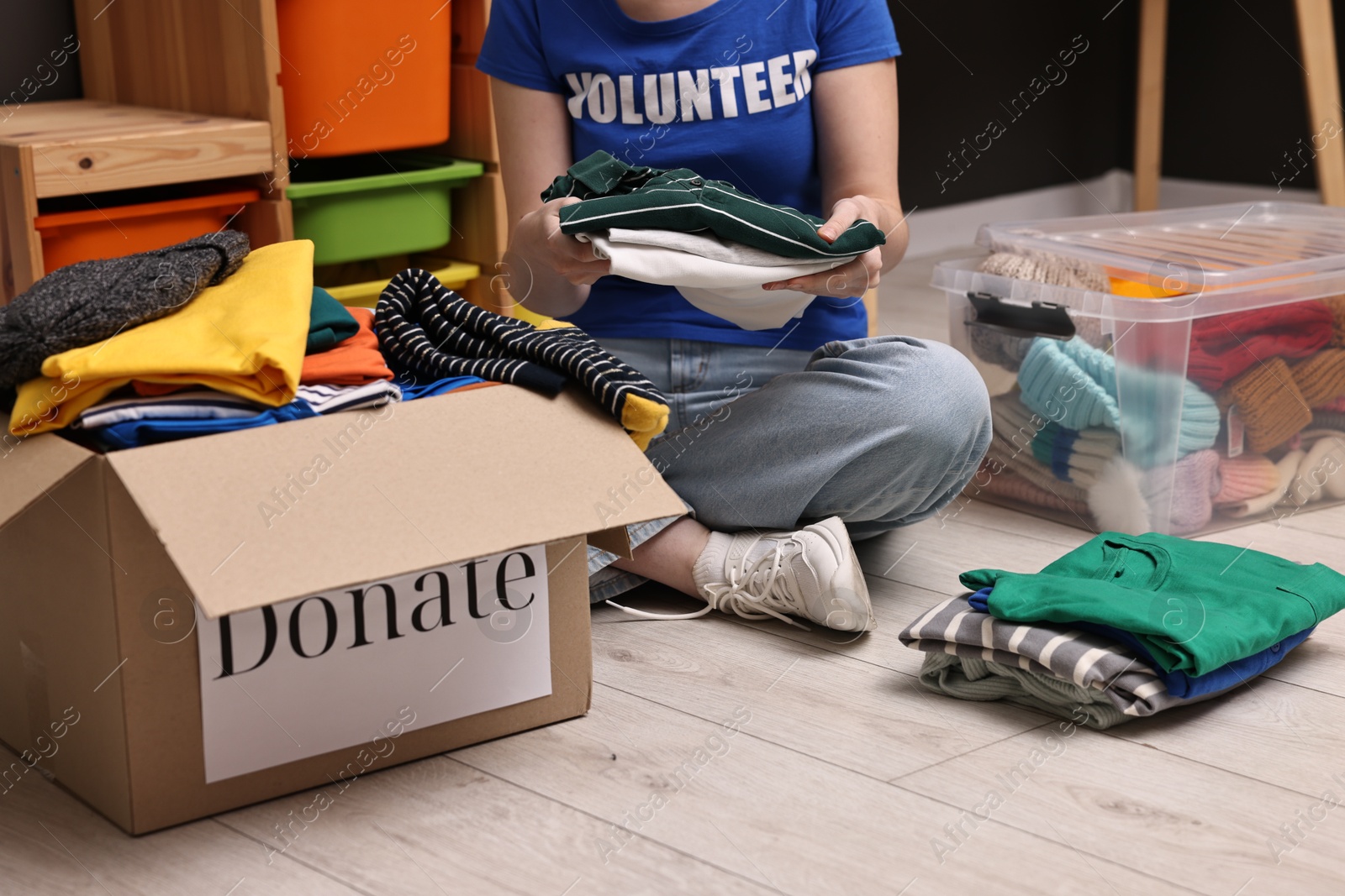 Photo of Volunteer sorting clothes for donation on floor indoors, closeup