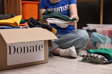 Photo of Volunteer putting clothes into donation box on floor indoors, closeup