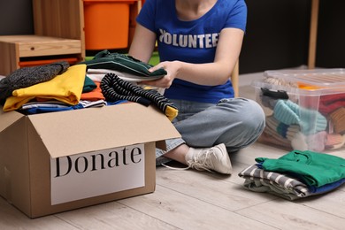 Photo of Volunteer putting clothes into donation box on floor indoors, closeup