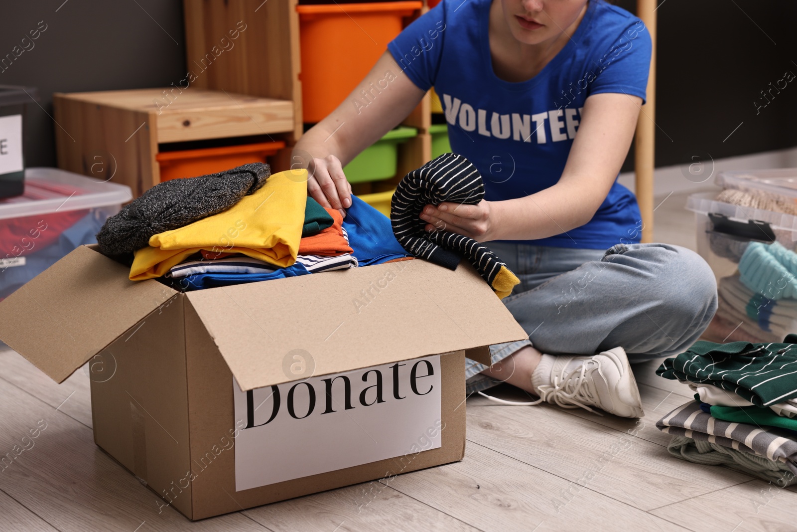 Photo of Volunteer putting clothes into donation box on floor indoors, closeup