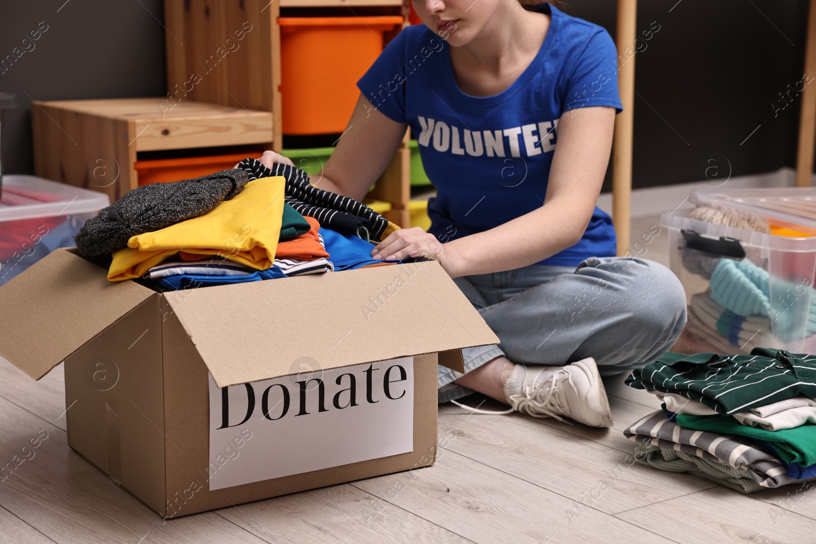 Photo of Volunteer putting clothes into donation box on floor indoors, closeup