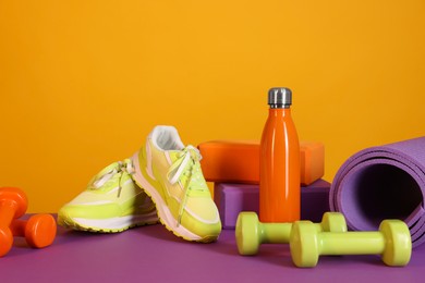 Stylish sneakers, thermo bottle and different sports equipment on color background