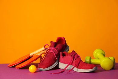 Stylish sneakers and different sports equipment on color background