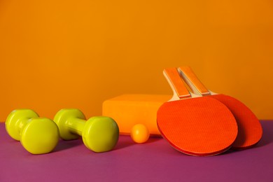 Dumbbells, yoga block, ping pong rackets and ball on color background