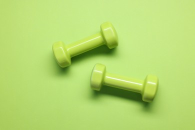 Two dumbbells on light green background, top view