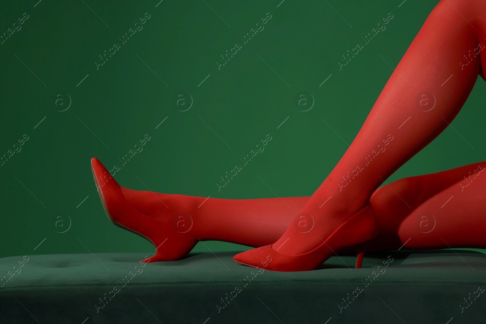 Photo of Woman in red tights and heels showing legs on green background, closeup