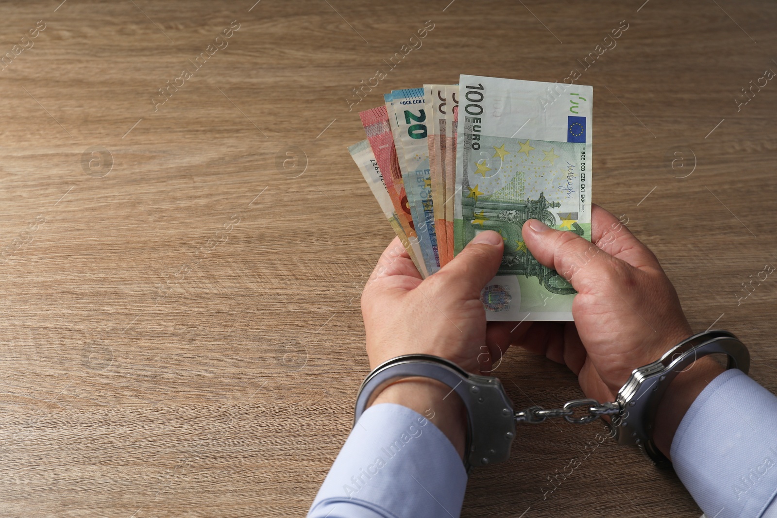 Photo of Corruption. Man in handcuffs holding euro banknotes at wooden table, closeup. Space for text