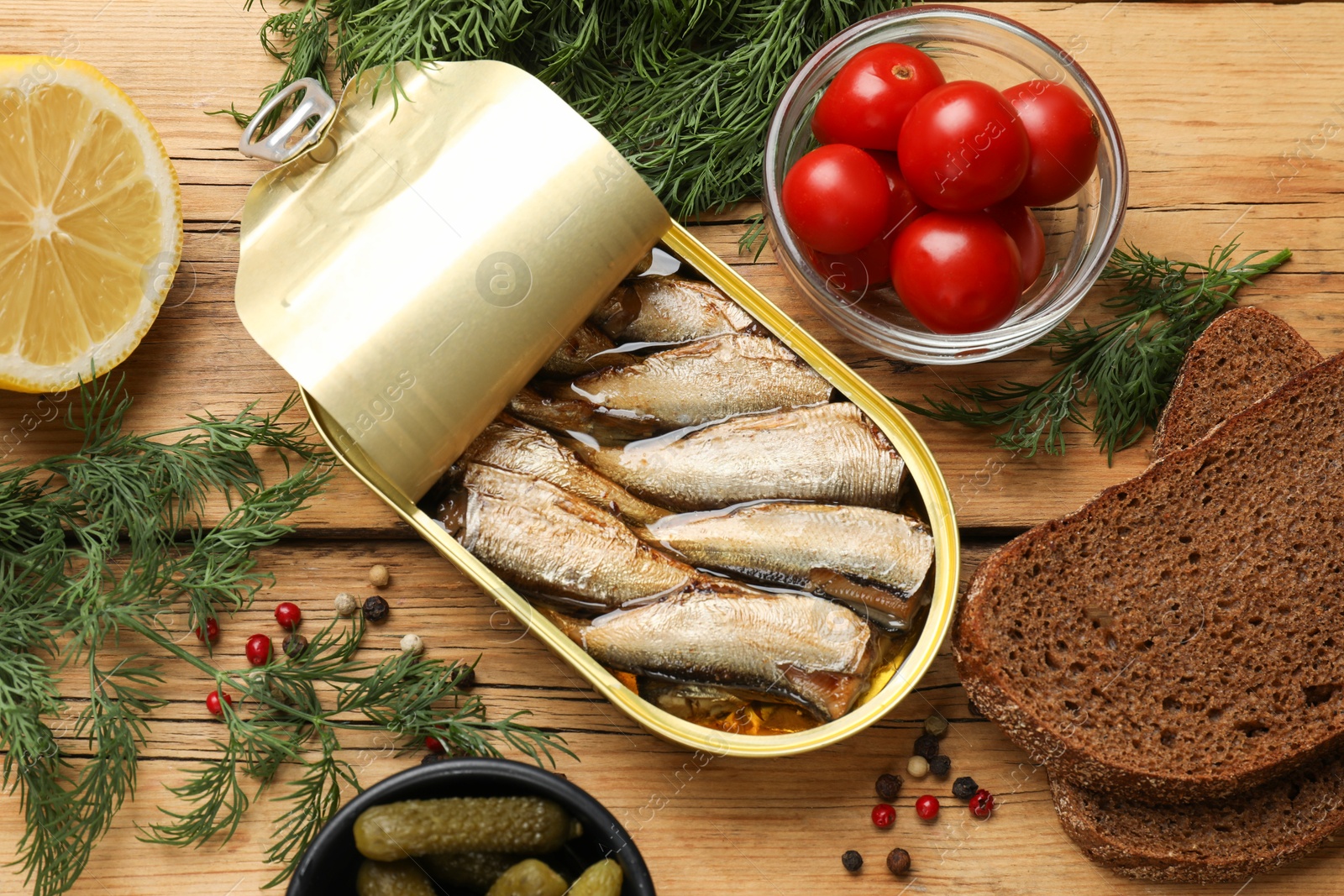 Photo of Tasty sprats in tin can served on wooden table, flat lay