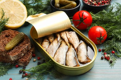 Photo of Tasty sprats in tin can served on light blue wooden table, closeup