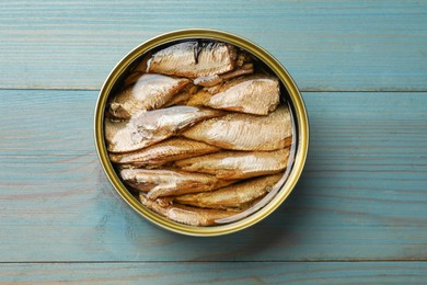 Photo of Tasty sprats in tin can on light blue wooden table, top view