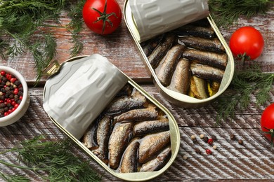 Photo of Tasty sprats in tin cans served on wooden table, flat lay