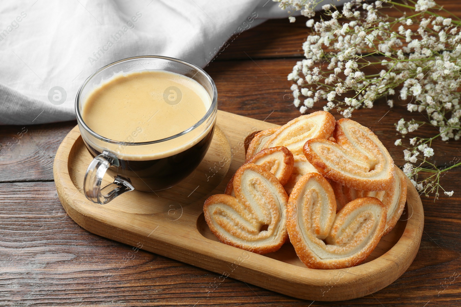 Photo of Tasty french palmier cookies, coffee and gypsophila flowers on wooden table, closeup