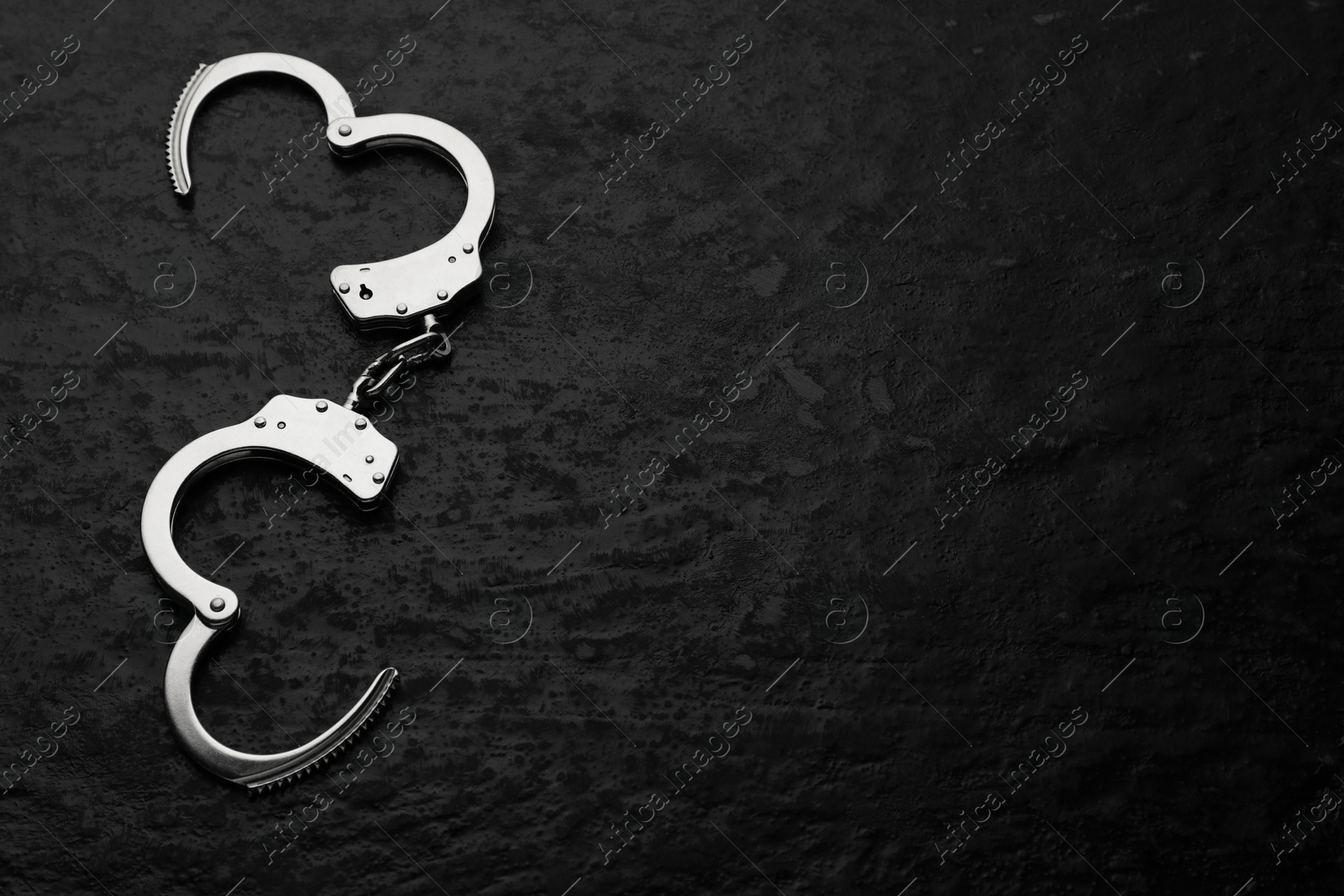 Photo of Metal chain handcuffs on black table, top view. Space for text