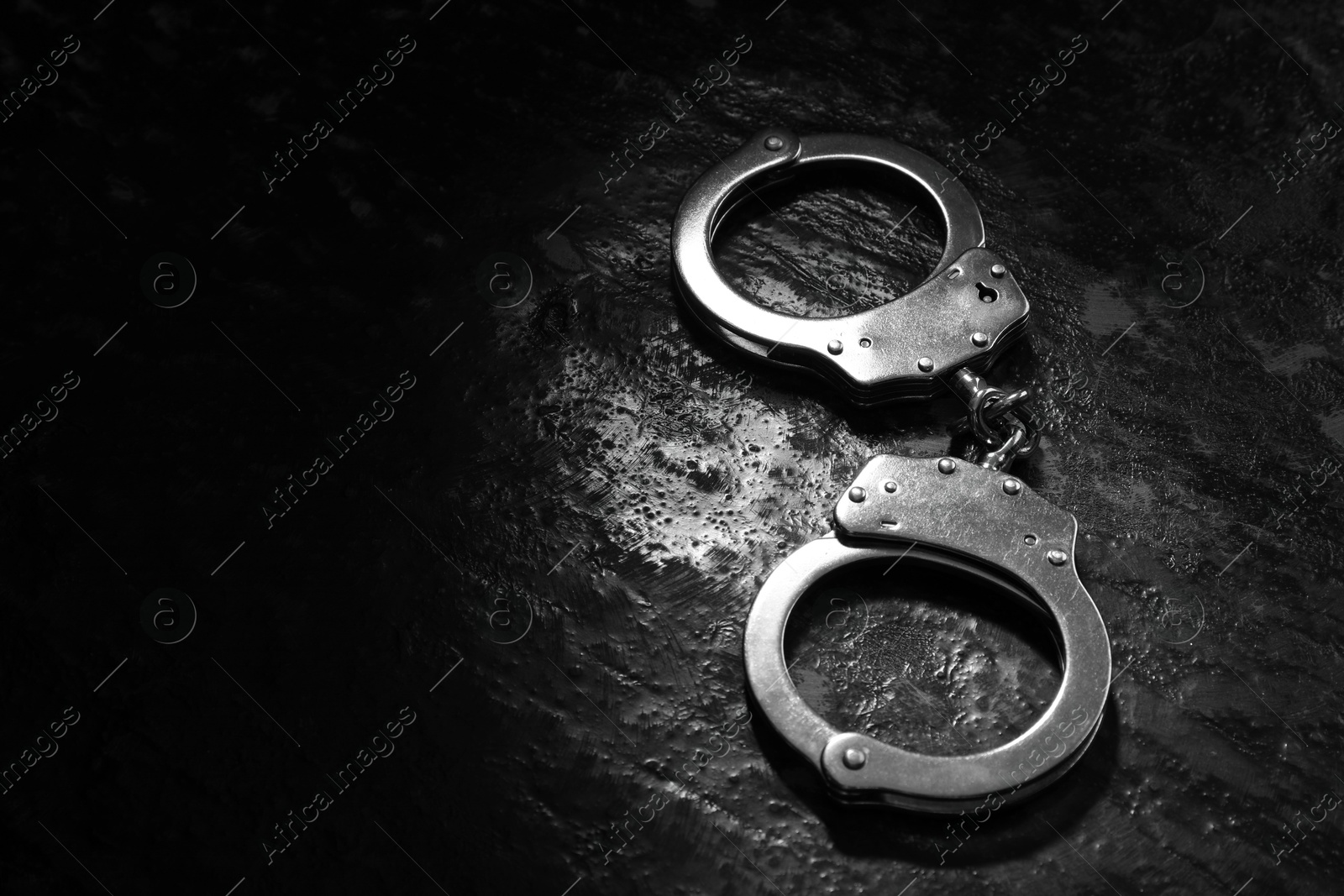 Photo of Metal chain handcuffs on black table, closeup. Space for text