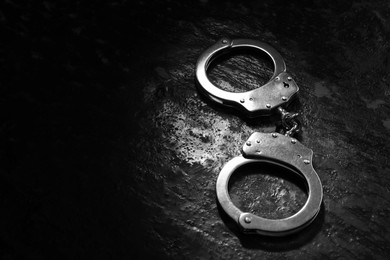 Photo of Metal chain handcuffs on black table, closeup. Space for text