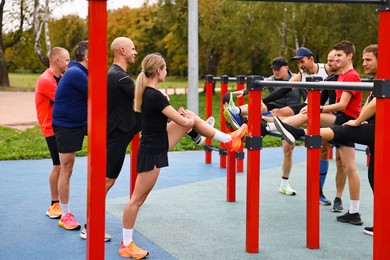 Photo of Group of people stretching near outdoor equipment in park. Healthy lifestyle