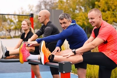 Photo of Group of people stretching near outdoor equipment in park. Healthy lifestyle