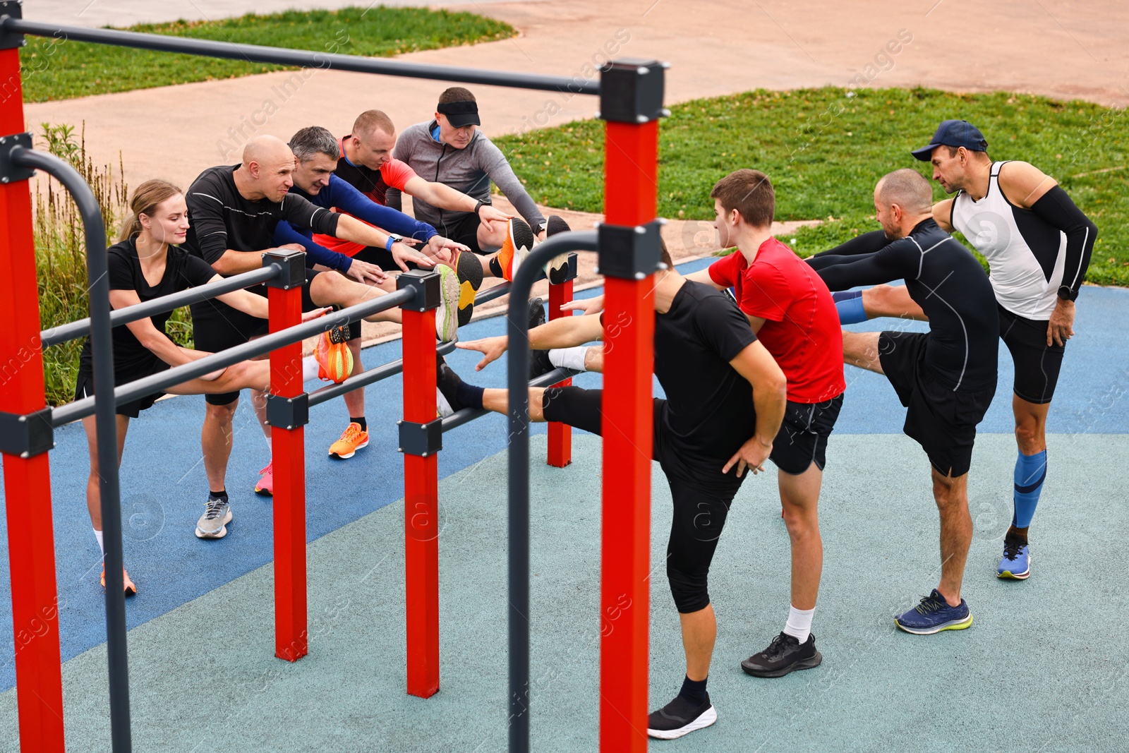 Photo of Group of people stretching near outdoor equipment in park. Healthy lifestyle