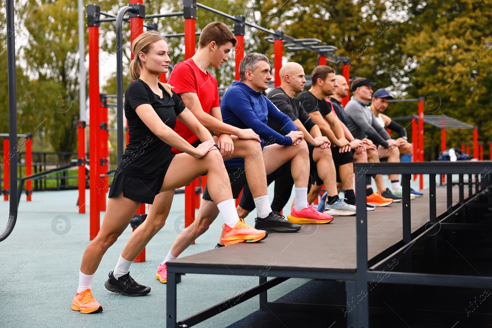 Photo of Group of people stretching near outdoor equipment in park. Healthy lifestyle