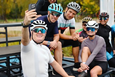 Photo of Group of athletic people with helmets and bicycles taking selfie outdoors