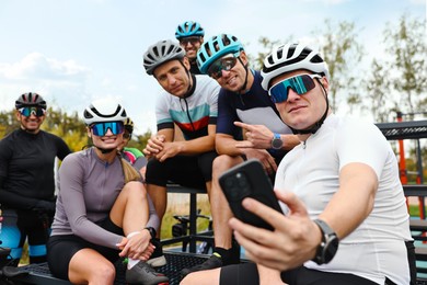 Photo of Group of athletic people with helmets and bicycles taking selfie outdoors