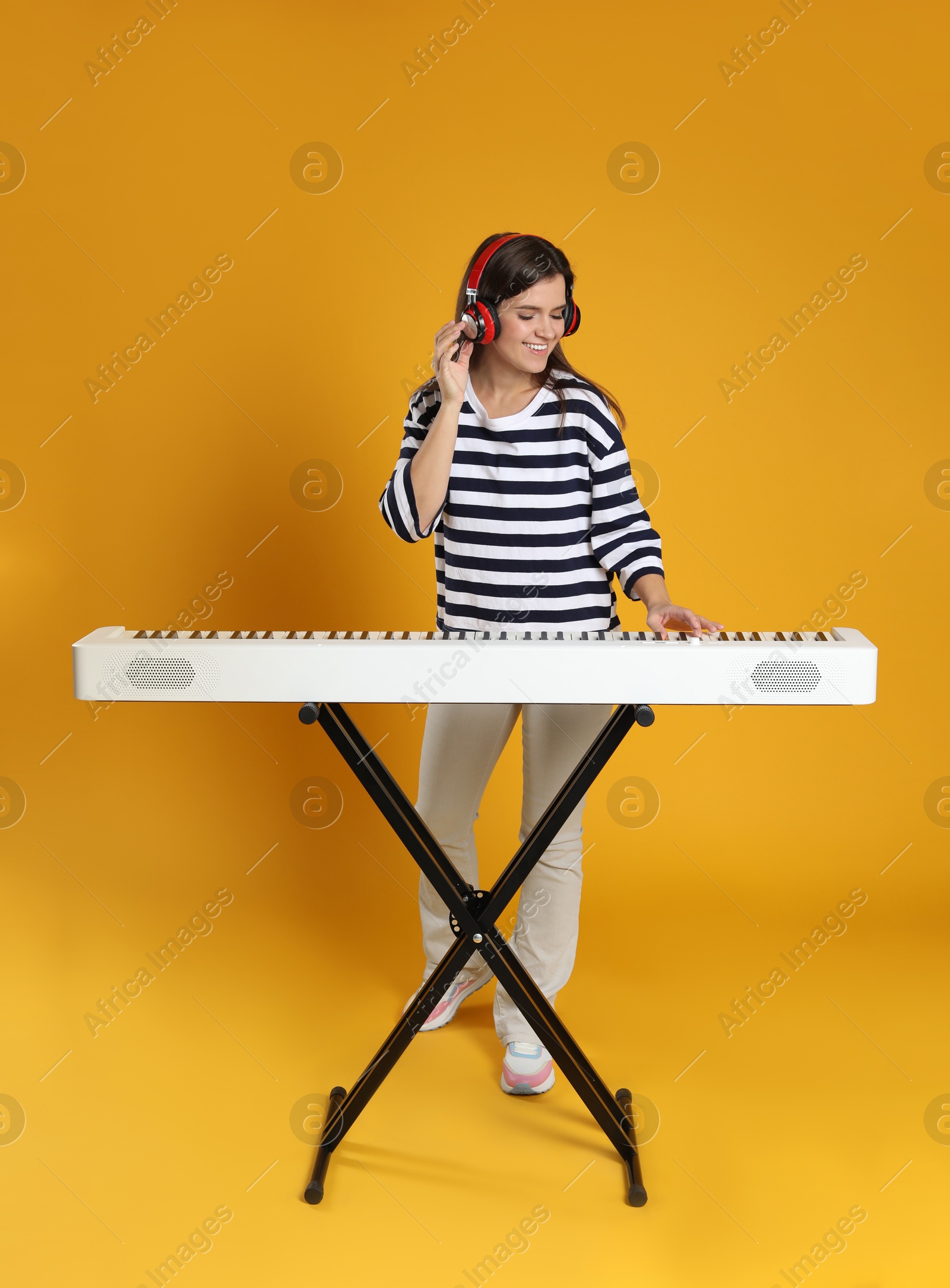 Photo of Smiling woman in headphones playing synthesizer on orange background